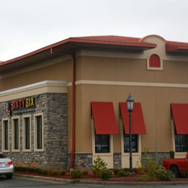 Exterior of Sixty Six Grill & Tap House with stone facade, red awnings, and a red roof.
