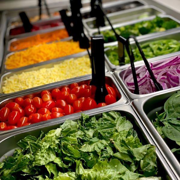 Close-up of a salad bar with fresh lettuce, cherry tomatoes, shredded cheese, and red onions.