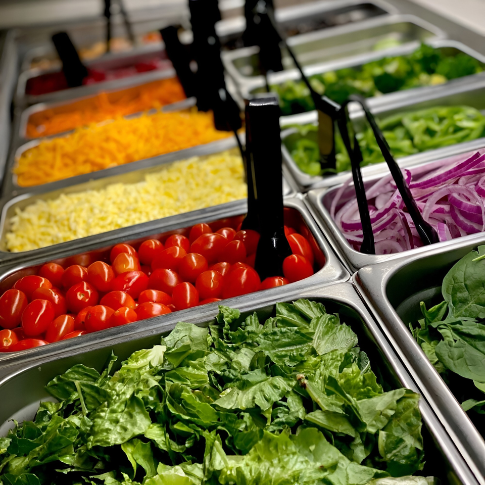 Close-up of a salad bar with fresh lettuce, cherry tomatoes, shredded cheese, and red onions.