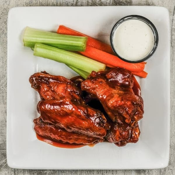 Sixty Six Grill & Tap House's American-style chicken wings, celery, carrots, and ranch dip on a white plate.