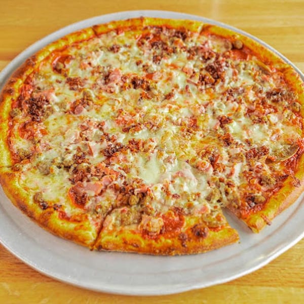 A whole meat lover's pizza with a slice removed, on a white plate at Sixty Six Grill & Tap House.