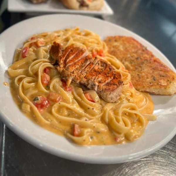 Creamy pasta with sliced grilled chicken and a side of garlic bread on a white plate.