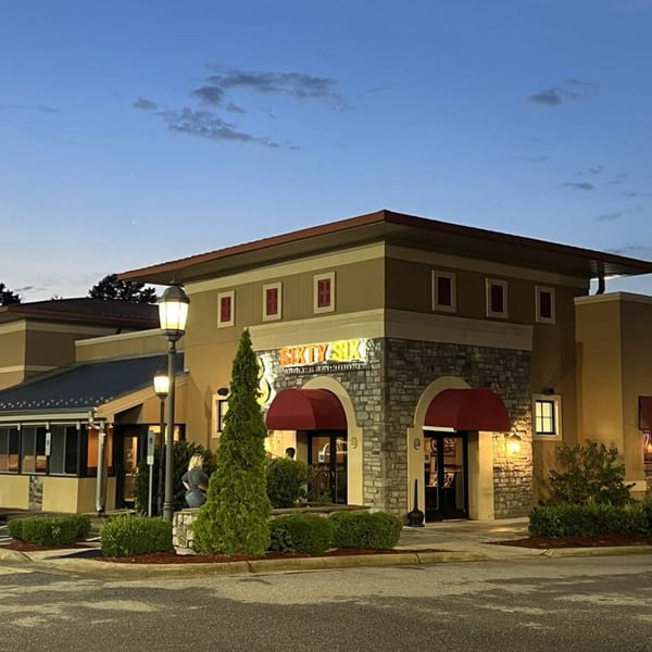 Exterior of Sixty Six Grill & Tap House at dusk, with illuminated sign, red awnings, and stone facade.