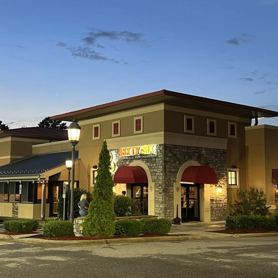 Exterior of Sixty Six Grill & Tap House at dusk, with illuminated sign, red awnings, and stone facade.