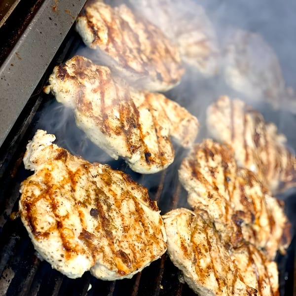 Chicken breasts with grill marks cooking on a smoky grill at Sixty Six Grill & Tap House.