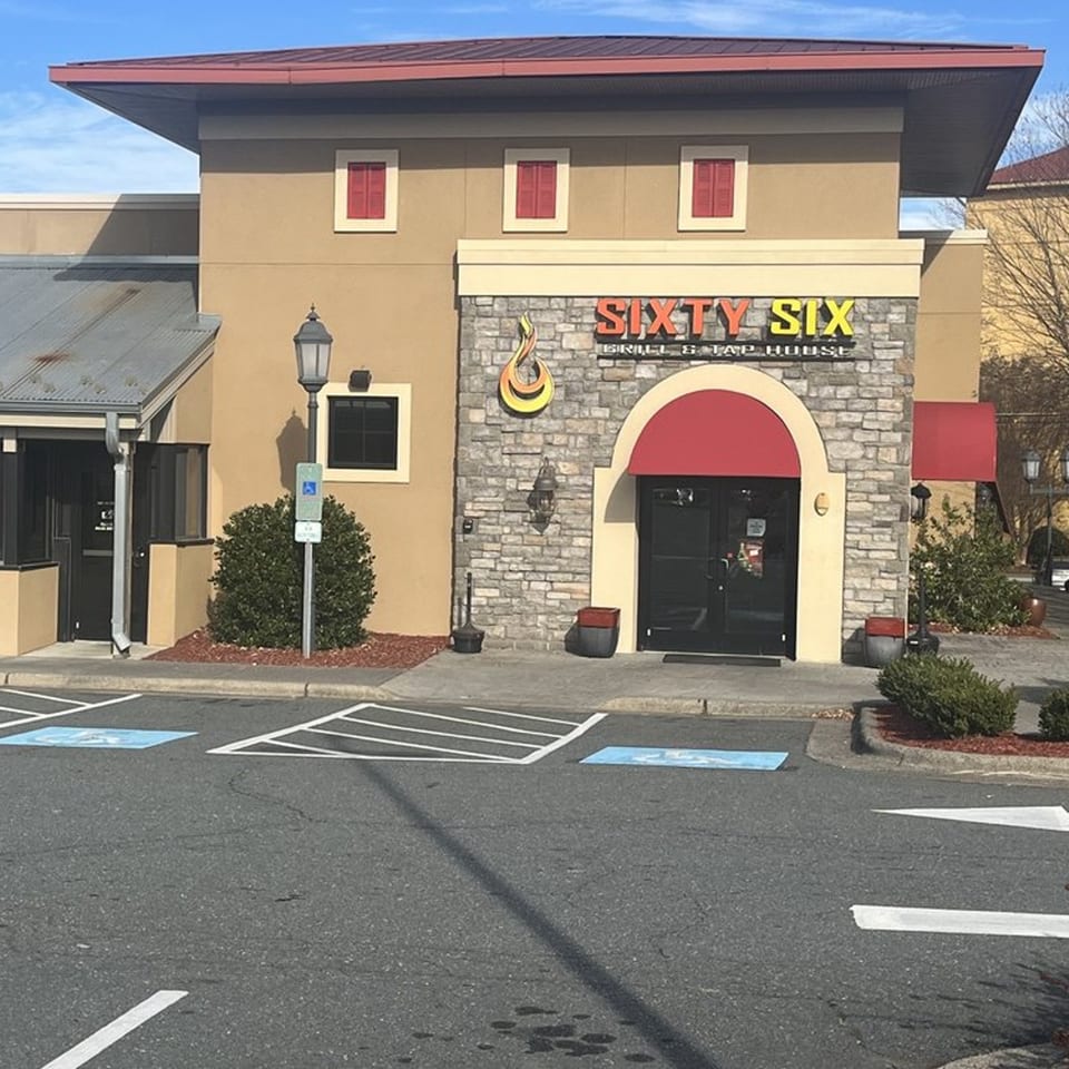Exterior of Sixty Six Grill & Tap House with a stone facade, red awnings, and parking spaces.