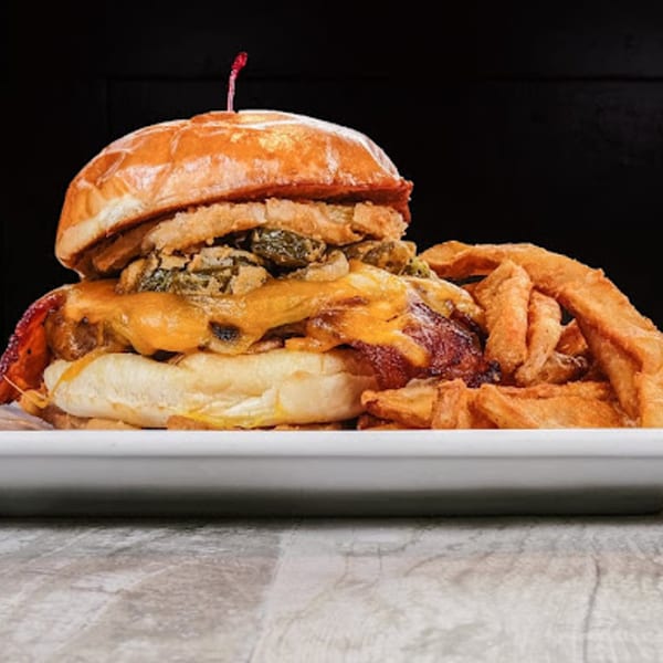 A Sixty Six Grill & Tap House burger with cheese, bacon, mushrooms, and fried onions, served with fries.